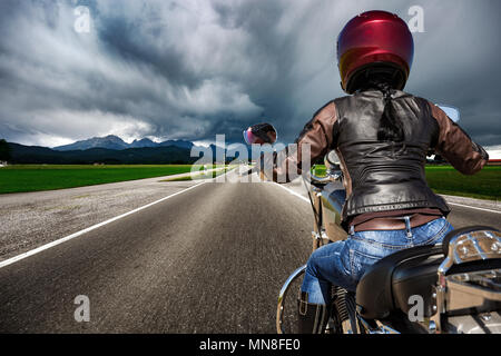 Biker Mädchen auf einem Motorrad die Straße hinunter in ein Gewitter - Forggensee und Schwangau, Deutschland Bayern rast Stockfoto