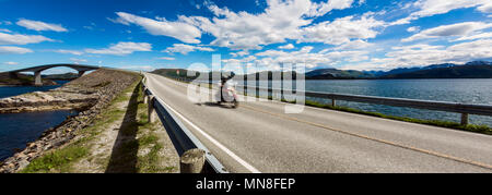 Biker fährt eine Straße mit Atlantik Straße in Norwegen. Atlantik Straße oder den Atlantik Straße (atlanterhavsveien) den Titel als Norwegischen Bau des Jahrhunderts" ausgezeichnet worden. Biker in motion blur". Stockfoto