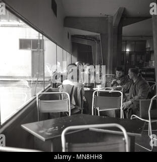 1950er Jahre, die Eltern sitzen im Gespräch in ein Hallenbad caferteria, neben dem Fenster heraus auf ein Open air Swimmingpool, England, UK. Stockfoto