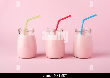 Drei Glasflaschen von Obst Joghurt mit bunten Pailletten auf dem Pastell rosa Hintergrund. Minimalistischer Stil, Seitenansicht. Gesunder Lebensstil Stockfoto