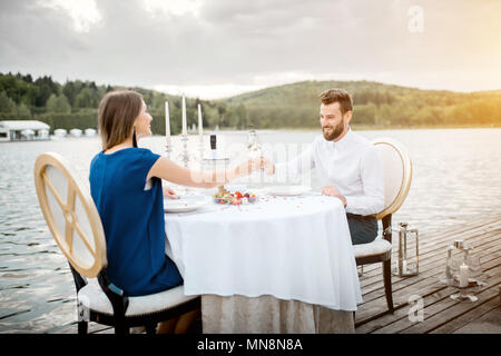 Elegantes Paar für ein romantisches Abendessen sitzen am Brunnen dekorierten Tisch in der Nähe des Sees auf dem Holzsteg mit Kerzen Stockfoto