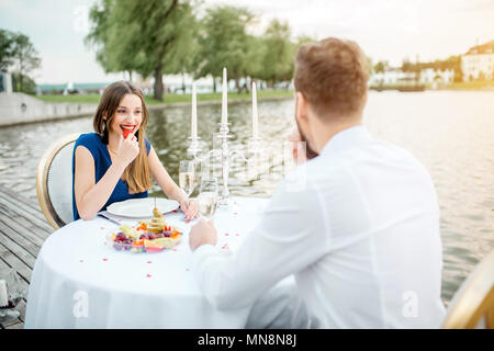 Elegantes Paar für ein romantisches Abendessen sitzen am Brunnen dekorierten Tisch in der Nähe des Sees auf dem Holzsteg mit Kerzen Stockfoto