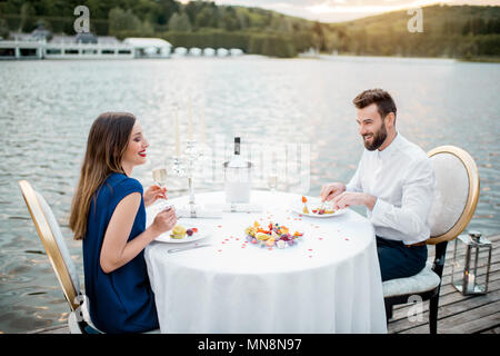 Elegantes Paar für ein romantisches Abendessen sitzen am Brunnen dekorierten Tisch in der Nähe des Sees auf dem Holzsteg mit Kerzen Stockfoto