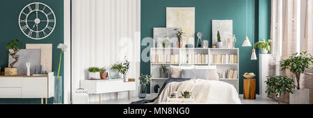 Viele Bücher auf weißem Holz- Rack im grünen Zimmer mit Doppelbett, Gemälde und Einrichtung Stockfoto