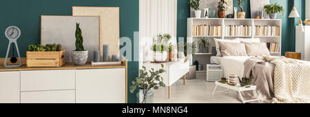 Frische Topfpflanzen in Grün offener Raum, Schlafzimmer mit Doppelbett, Bücher auf weißem Rack und moderne Gemälde Stockfoto