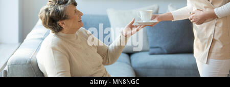 Betreuer geben eine Tasse Tee zu einem Lächeln alte Dame während eines Aufenthalts im Hospiz Stockfoto