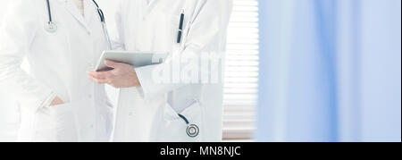 Nahaufnahme von einem Arzt im weißen Kittel mit Stethoskop Holding eine Tablette, die Beratung zu einem Fall mit einem Kollegen in hellen Krankenhaus Stockfoto