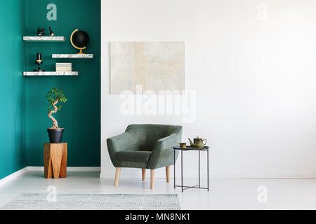 Minimalistische Einrichtung in Weiß und Grün mit Sessel, Teekanne, Anlage auf einem Holztisch und Marmor Bücherregale Stockfoto