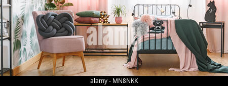 Zwei graue und rosa Pompoms hängend auf einer Metal bed Frame in gemütlichen Schlafzimmer Innenraum mit Knoten Sitzkissen Sessel Stockfoto