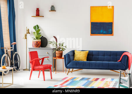 Red Chair und Royal Blue Lounge im hellen Wohnzimmer Einrichtung mit bunten Teppich, moderne Kunst Malerei, Frische Pflanzen und gold Lampe neben g Stockfoto