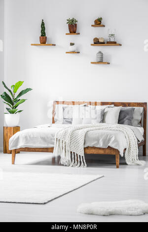 Anlage auf hölzernen Hocker neben dem Bett mit Stricken Decke in einfachen weißen Schlafzimmer Innenraum Stockfoto