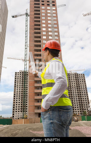 Ansicht von hinten Bild der männlichen Architekt in hardhat Holding Blueprints und zeigen auf der Baustelle Stockfoto