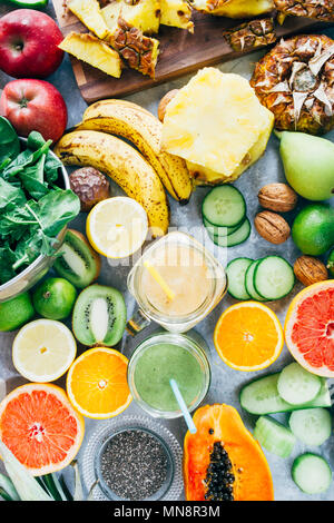 Gesunde Mango und grüner Smoothie detox Drink in ein Glas von rohem Obst Zutaten, Banane, Ananas, Papaya, Gurken, Kohl, Spinat umgeben, Stockfoto