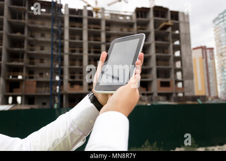 Closeup Image der jungen Mann im weißen Hemd mit digitalen Tablette gegen Gebäude im Bau. Sie können das Bild auf dem Bildschirm einfügen Stockfoto