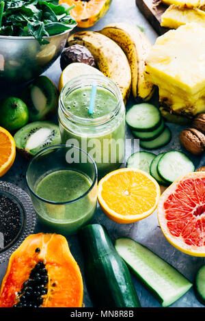 Gesunden grünen Smoothie detox Drink in ein Glas von rohem Obst Zutaten, Banane, Ananas, Papaya, Gurken, Kohl, Spinat umgeben, Stockfoto
