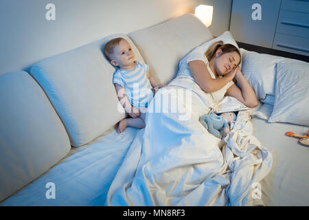 9 motnhs Alte schlaflose Babysitting auf Bett neben schlafenden Jungen Mutter Stockfoto