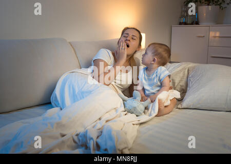 Cute Baby Boy im Bett sitzen und sein müdes Gähnen Mutter Stockfoto