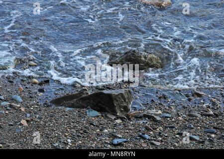 Sanfte Wellen gegen kleine Felsen auf einer peddle Strand an einem sonnigen Tag. Stockfoto