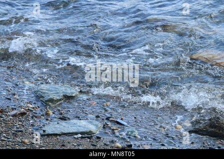 Sanfte Wellen gegen kleine Felsen auf einer peddle Strand an einem sonnigen Tag. Stockfoto