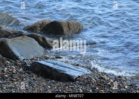 Sanfte Wellen gegen kleine Felsen auf einer peddle Strand an einem sonnigen Tag. Stockfoto