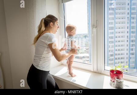 Mutter hetzen, um zu Ihrem baby boy auf der Fensterbank. Konzept der Baby in Gefahr Stockfoto