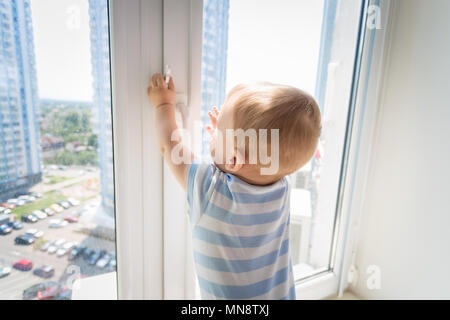 9 Monate alte baby boy steht auf fensterbrett und versuchen, das Fenster zu öffnen. Bbay in Gefahr Stockfoto