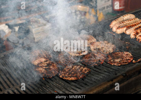 Burger auf einem offenen Grill zubereitet, mit viel Rauch aus Gießen. Stockfoto