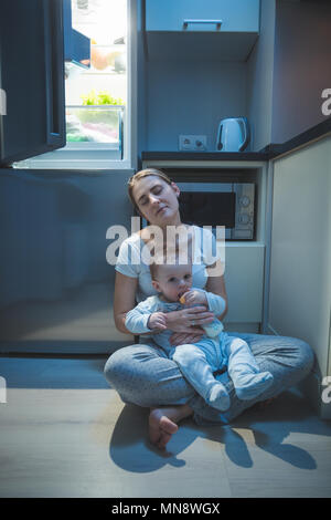 Schläfrig, müde Frau sitzt Küche Etage in der Nacht und Ihr Baby füttern mit Milch Stockfoto