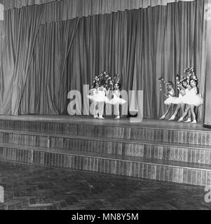 1965, junge Mädchen, die eine Ballettaufführung auf einen Vorhang hinter der Bühne aus Holz in einer Schule Hall, England, UK. Stockfoto