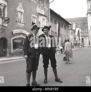 1950er Jahre, Deutschland, zwei Männer zusammen draußen auf der Straße stand das Tragen der traditionellen bayerischen Kleidung der Epoche, eine Form von Lederhosen, bekannt als Bundhosen. Hier sind sie elegant in die vollständige Outfit gekleidet, der knielange Hose mit Jacken und Mützen. Stockfoto