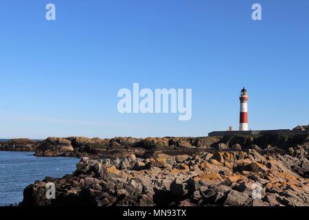 Rot-weiße Leuchtturm, gegen den wolkenlosen blauen Himmel mit weißen Geländer auf Brücke im Vordergrund. Stockfoto