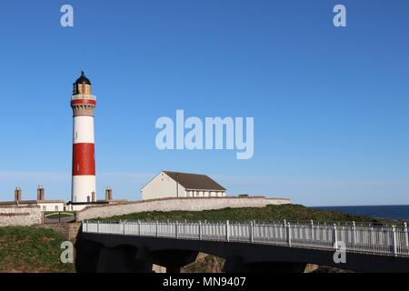 Rot-weiße Leuchtturm, gegen den wolkenlosen blauen Himmel mit weißen Geländer auf Brücke im Vordergrund. Stockfoto