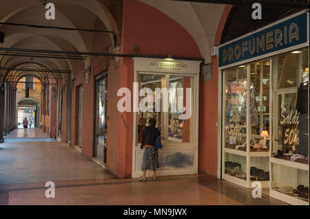 Bologna. Ältere Frau schaut in das Fenster eines Store, Arkaden der Strada Maggiore. Italien. Stockfoto