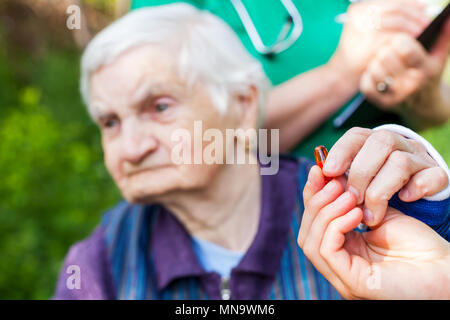 Ältere kranke Frau, die Pillen von Krankenschwester outdoor, Arzt schreiben ärztliche Verschreibung im Hintergrund Stockfoto