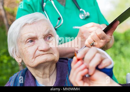 Ältere kranke Frau, die Pillen von Krankenschwester outdoor, Arzt schreiben ärztliche Verschreibung im Hintergrund Stockfoto