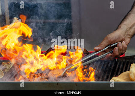 Grill Feuer mit Händen und Grill Zange Stockfoto