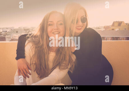 Lächeln und Spaß für eine blonde Mädchen Paar im Freien auf der Terrasse roodtop. Sonnenlicht Hintergrundbeleuchtung Bild mit Freundschaft Konzept. schöne Modelle h Stockfoto