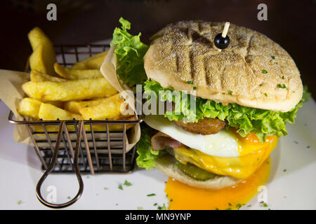 Ein Burger mit Pommes frites serviert. Die Burger verfügt über einen Zwiebelring, Spiegelei und Salat. Stockfoto