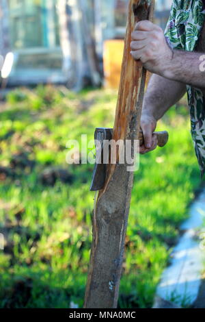 Ein Mann schneidet Holz mit einer Axt in den Garten. Stockfoto