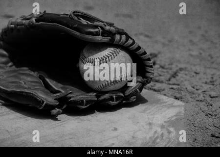 Schwarz und Weiß vintage Baseball in Spieler Handschuh Handauflegen Home Plate, ball Feld Schmutz im Hintergrund. Stockfoto