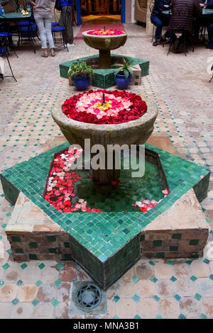 Dekorative, marokkanische Zimmerbrunnen voller rosa und roten Rosenblättern schwebend im Wasser Stockfoto