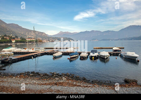 Ein friedlicher Blick auf die Boote, die an einem Jachthafen am Comer See, Italien, angedockt sind, umgeben von bergigem Gelände unter einem hellblauen Himmel. Como, Lombardei, Italien Stockfoto