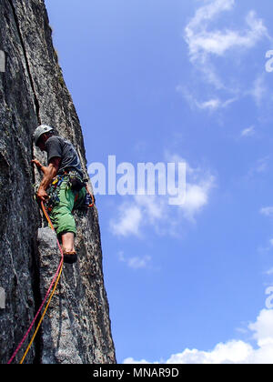 Kletterer in hellen Farben gekleidet auf einem steilen Granit Klettersteig in den Alpen Stockfoto