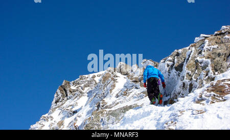 Männliche backcountry skier Wandern zu einer hochalpinen Gipfel in der Schweiz an einem Felsen und Snow Ridge im leichten Nebel Stockfoto