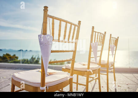 Hochzeit am Strand Ort Einrichtung mit modernem Stil von Gold chiavari Stühle mit Kegel von rosenblüte hängen und Licht der untergehenden Sonne direkt aus dem righ Seite Stockfoto