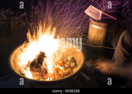 Brennenden Kamin mit viel hellen Funkeln in der Nacht. Lodernden Lagerfeuer mit kleinen Beil und Menschen Spuren im Hintergrund Stockfoto