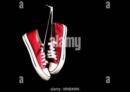 Rote sneakers Hängen auf schwarzem Hintergrund und Platz für Text oder Design auf der linken Seite. Retro Mode Stockfoto