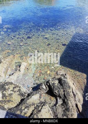 Klares Wasser, Felsen und Steine am Strand mit Reflexion im Wasser Stockfoto