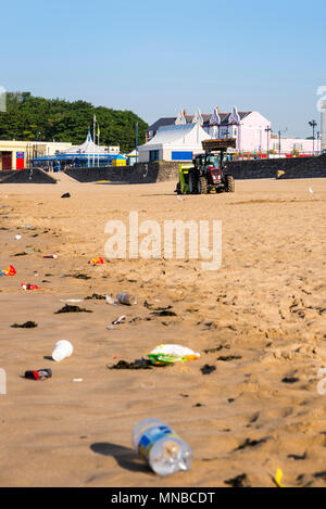 Vordergrund Wurf am ruhigen Sandstrand im Ferienort früh an einem hellen, sonnigen Sommermorgen durch Hintergrund Traktor mit surf Rechen gesäubert werden. Stockfoto