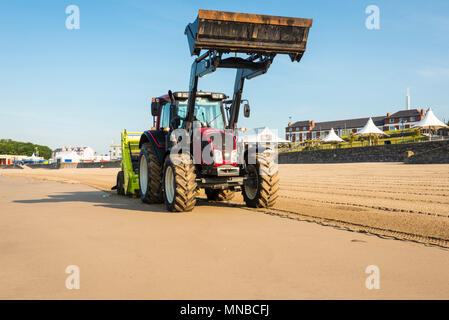 Whitmore Bay Beach bei Barry Island, Wales, früh an einem hellen, sonnigen Sommermorgen der Wurf durch einen roten Traktor ziehen einer Friseur Surfen Rechen gesäubert werden. Stockfoto